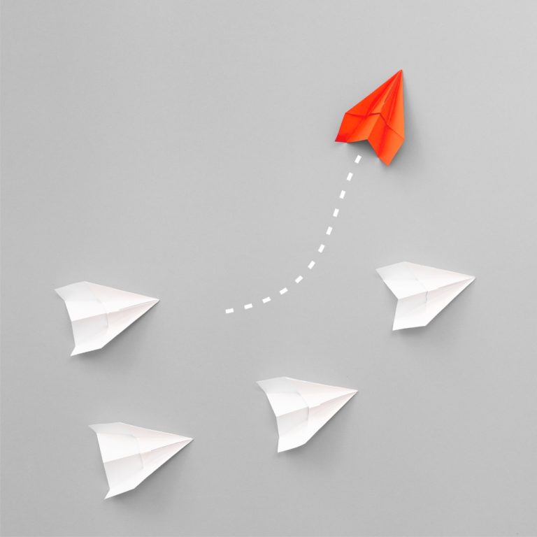 group of paper airplanes four whit and one red spearheading, symbolizing better solutions