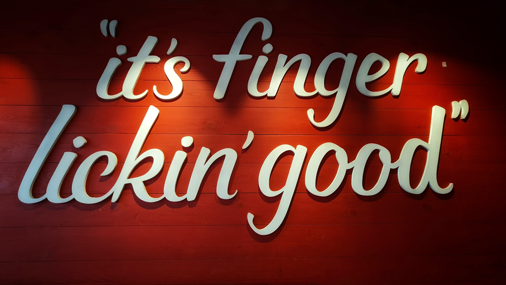 white KFC slogan It's finger lickin' good on a red wooden background