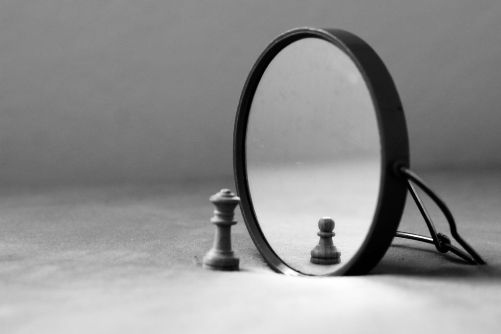 chess figurine in front of mirror. the reflection in the mirror is a smaller figurine. symbolizes mirror image and self perception