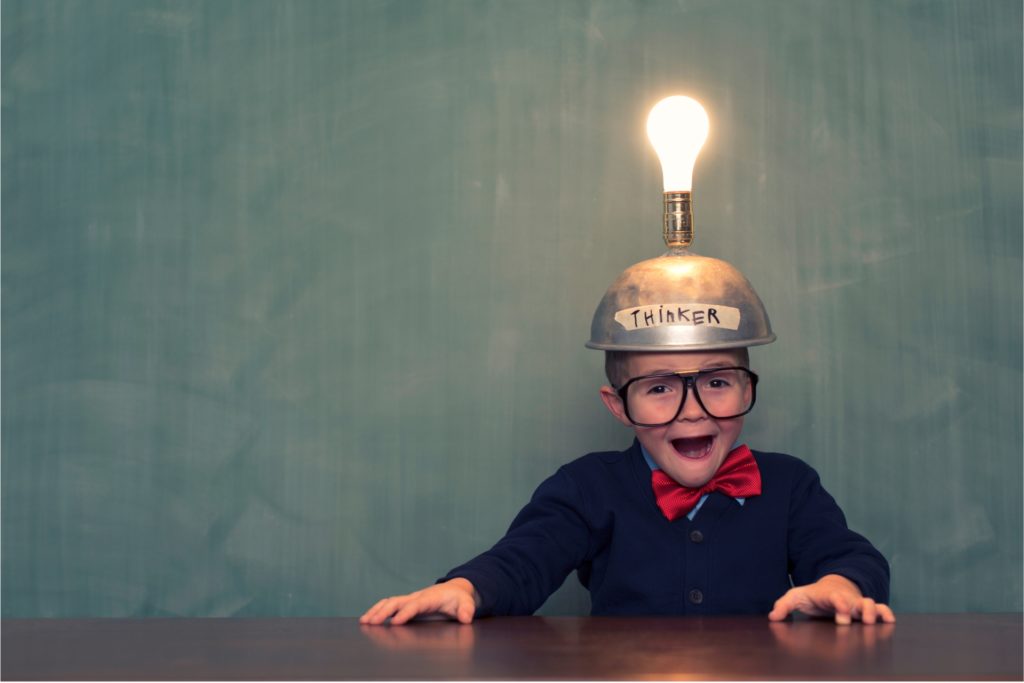 Young boy with big glasses wearing helmet written _thinker_ on it and a lighted lightbulb on top of it