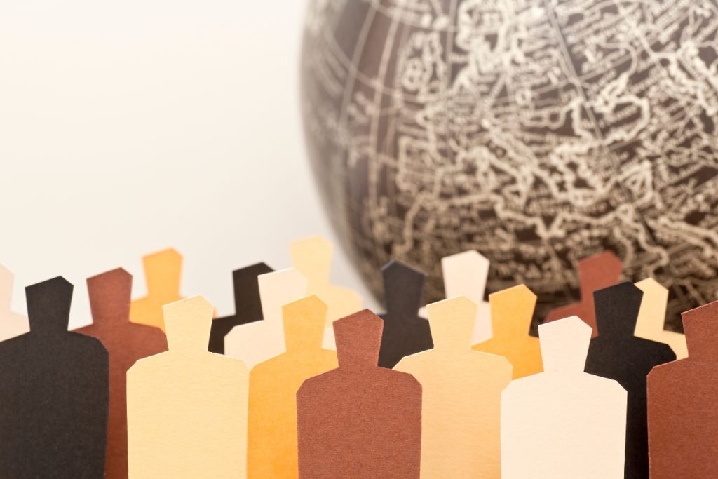 Cardboard figures representing diverse people in different hues of brown with a globe in the background. Symbolizes many cultures in a globalized world