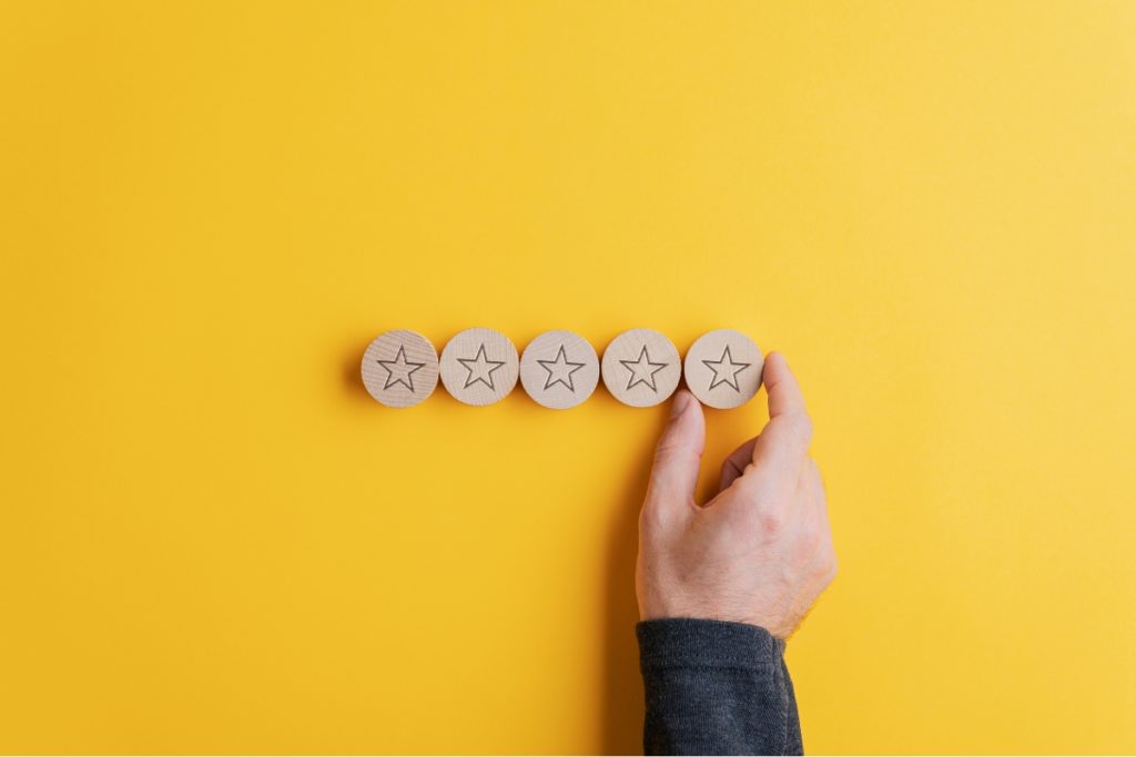 Male hand placing five wooden cut circles with stars on them in a row over bright yellow background. Conceptual image of Quality check in linguistic testing